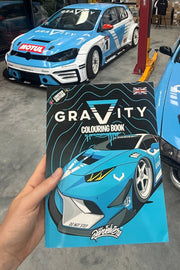 Person holding a 'GRAVITY' coloring book with a car design in front of a blue and white car.